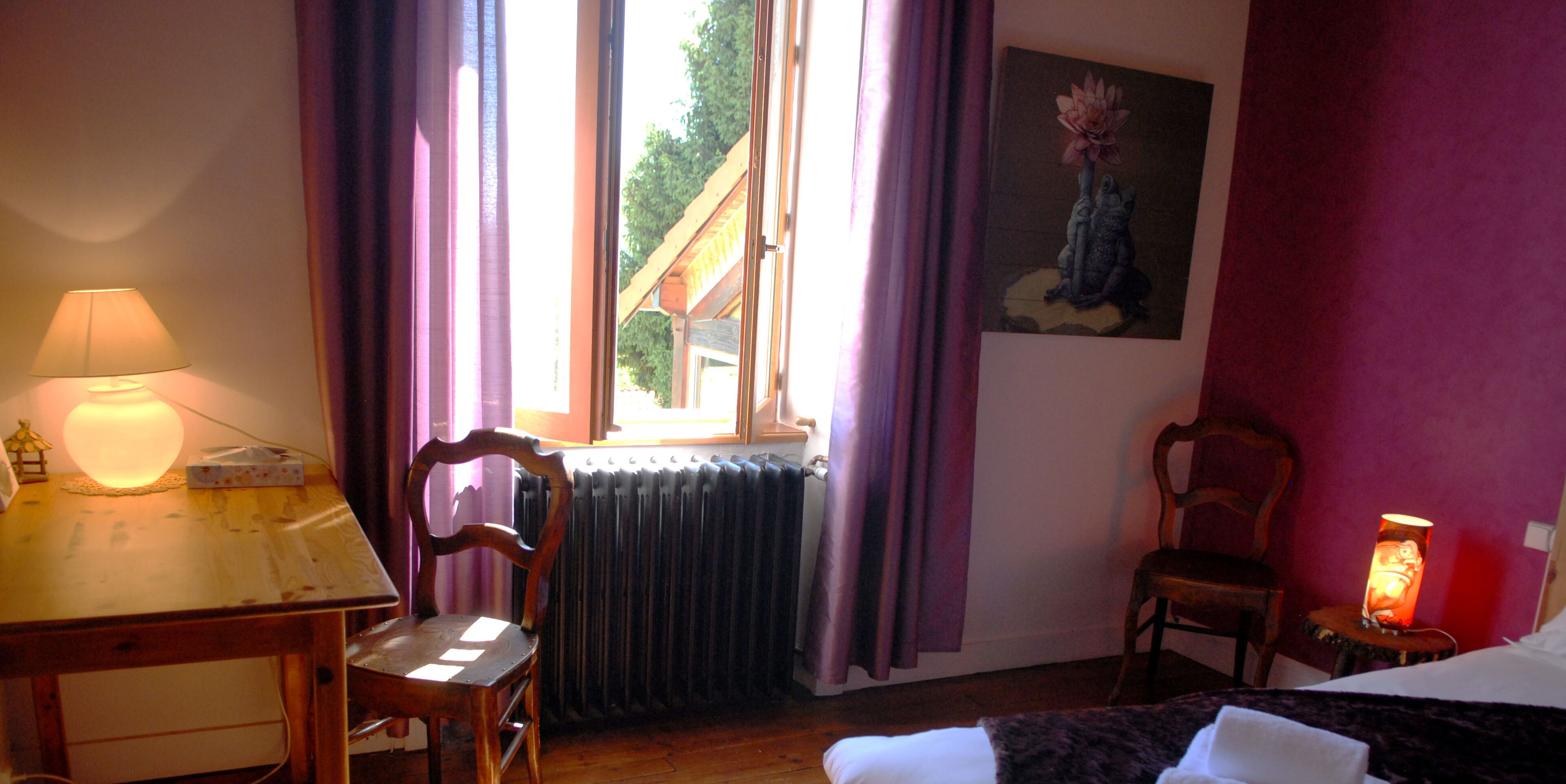 Une pièce comprenant un lit, un bureau avec une lampe, une chaise, un radiateur et une fenêtre avec des rideaux.