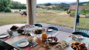 A dining table set for breakfast with a scenic view, including croissants, bread, cheese, and a pitcher of water.