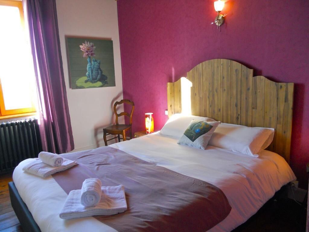 Quarto de hotel com cama, uma cadeira, luminária na parede e um quadro.