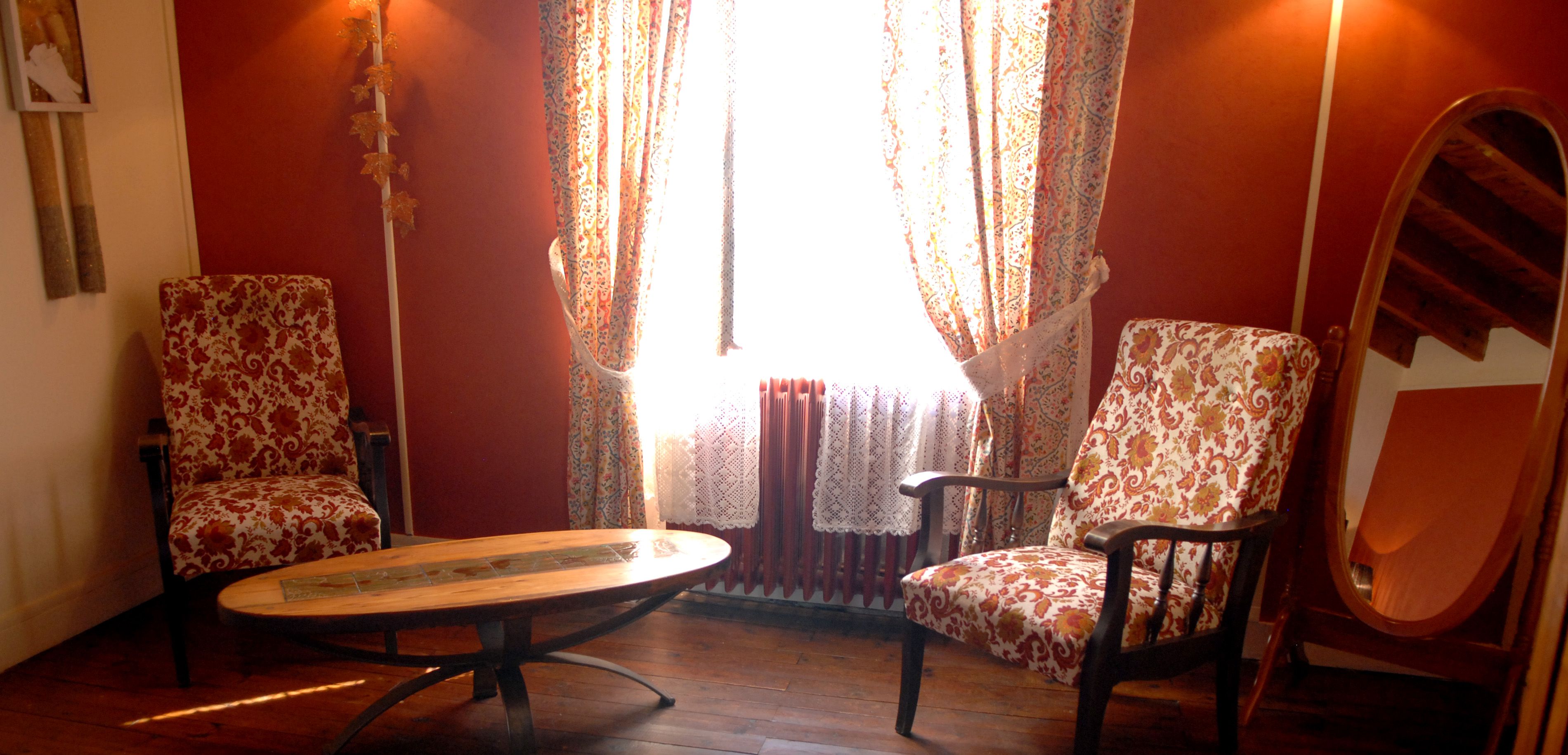 A room with two patterned armchairs, a wooden table, and a mirror on the wall.