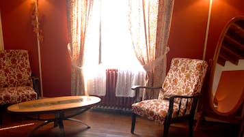 A room with two patterned armchairs, a wooden table, and a mirror on the wall.