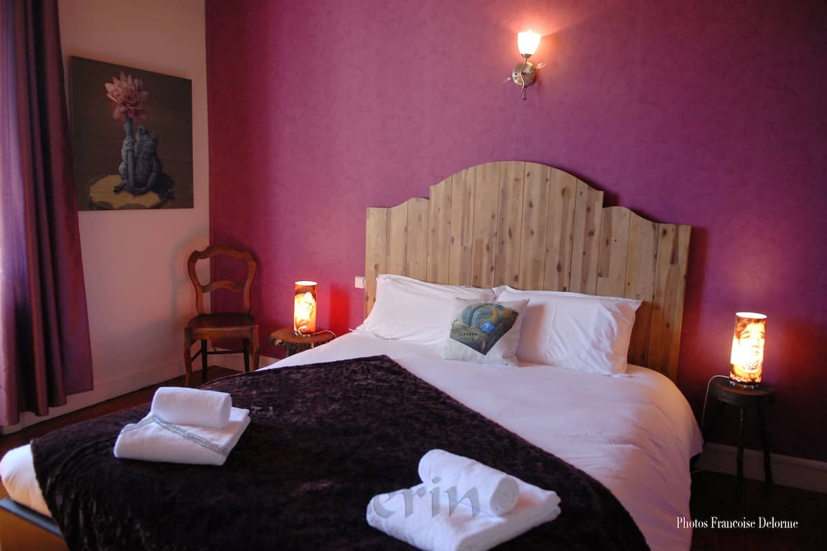 Habitación de hotel con cabecera de madera, una cama grande con ropa blanca, un plaid oscuro y dos lámparas de noche.
