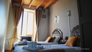 A bedroom with a wooden ceiling, a bed with multiple pillows, a nightstand, and a window with curtains.