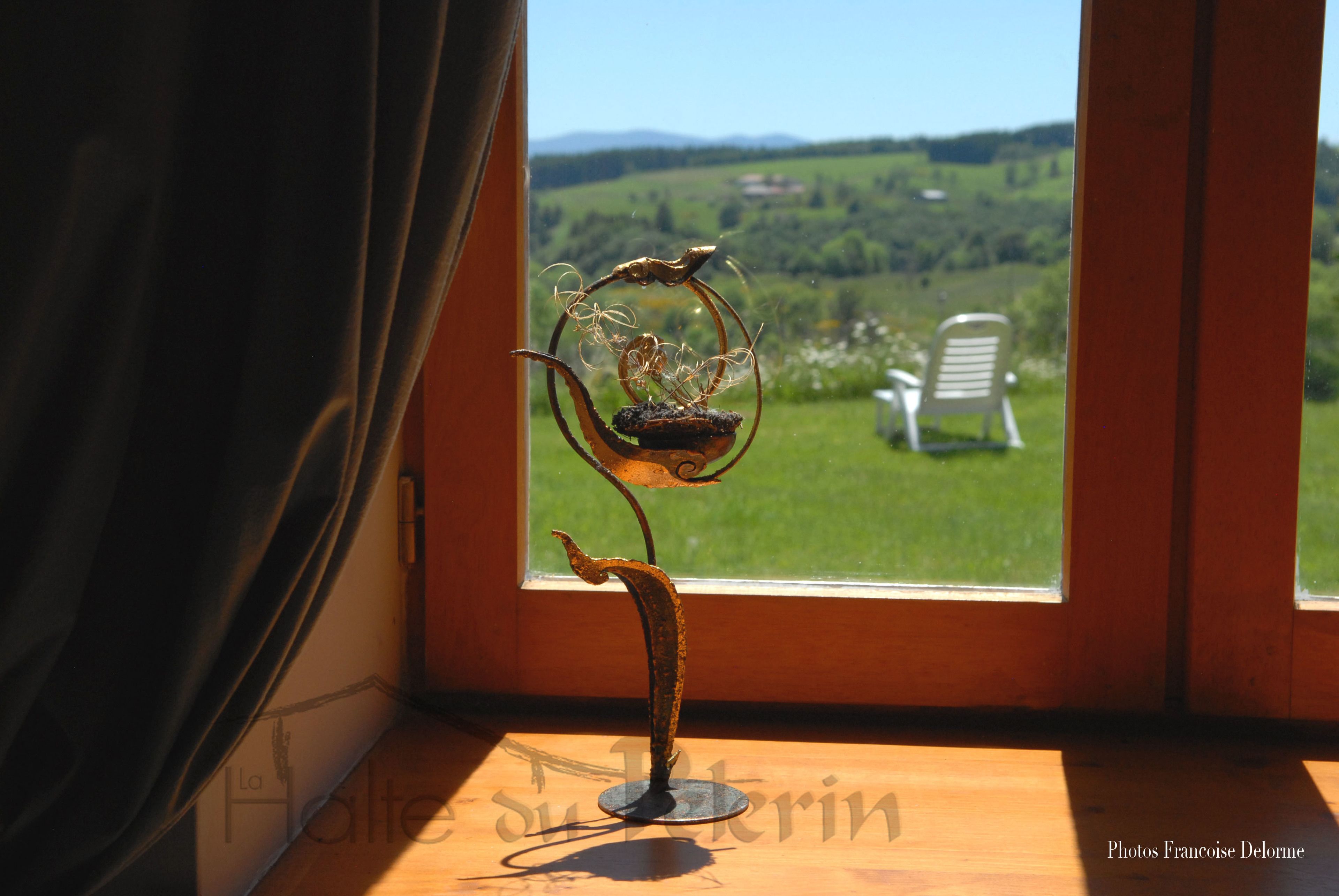 A metal sculpture on a windowsill with a view of a green landscape and a chair outside.