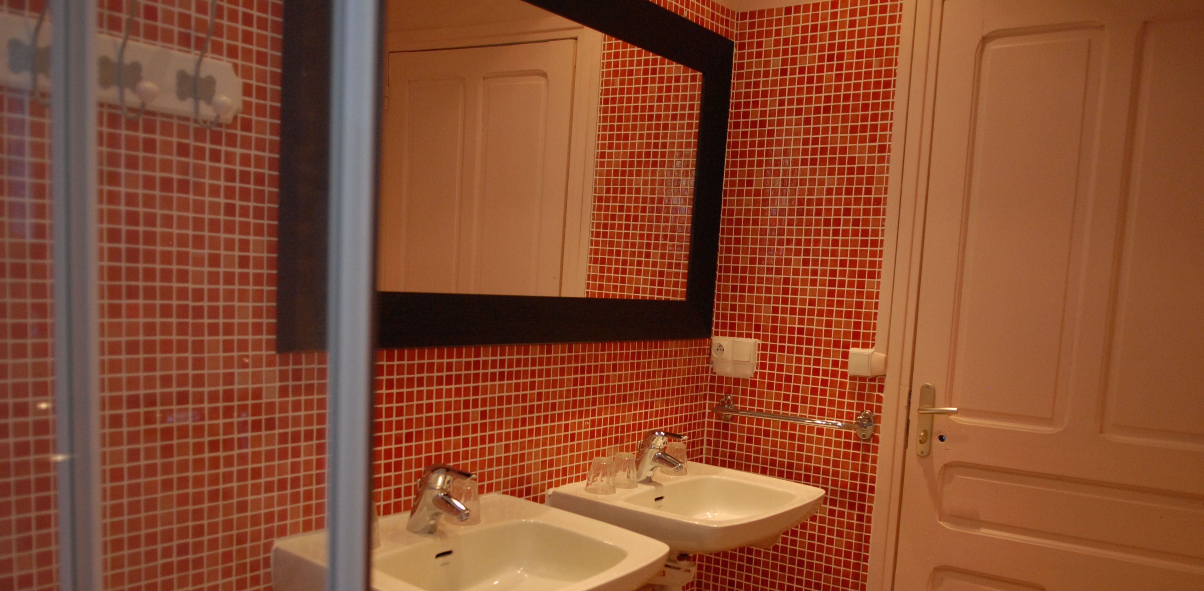 Un baño con paredes de baldosas rojas, dos lavamanos, un espejo y una puerta.