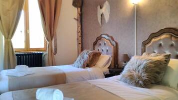 Ein Hotelzimmer mit zwei Betten, jedes mit einem zusammengerollten Handtuch. Es gibt einen Heizkörper, eine Wandleuchte und einen dekorativen Gegenstand, der einem Engelsflügel ähnelt.