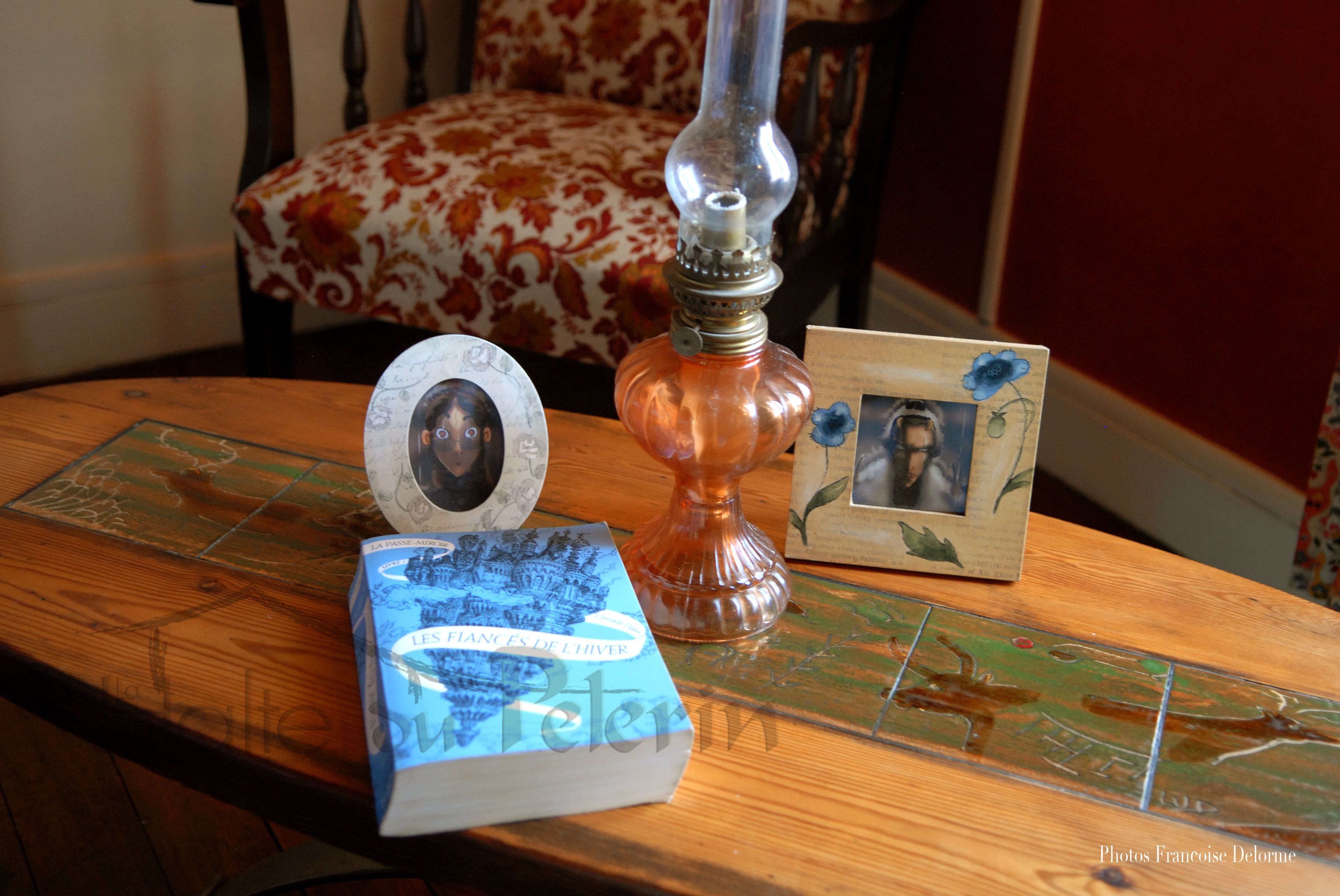 A wooden table with a book titled 'Les fiances de l'amour', a decorative lamp, and a framed photograph.