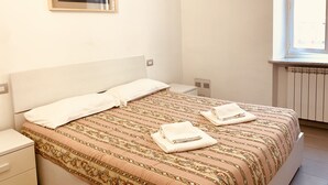 A neatly made bed with a patterned bedspread, a white pillow, and two folded towels on the bed. There is a framed picture on the wall above the bed. - Appartamenti St'Andrea (Levanto)