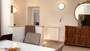 A modern living room with a white dining table, two chairs, a wooden cabinet with a television, and a large mirror on the wall. - Appartamenti St'Andrea (Levanto)