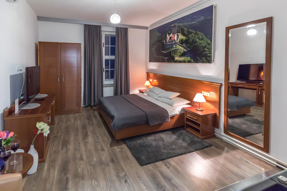 Hotelkamer met een bed, nachtkastjes, een kledingkast, een bureau met een computer, een spiegel en een raam met gordijnen.