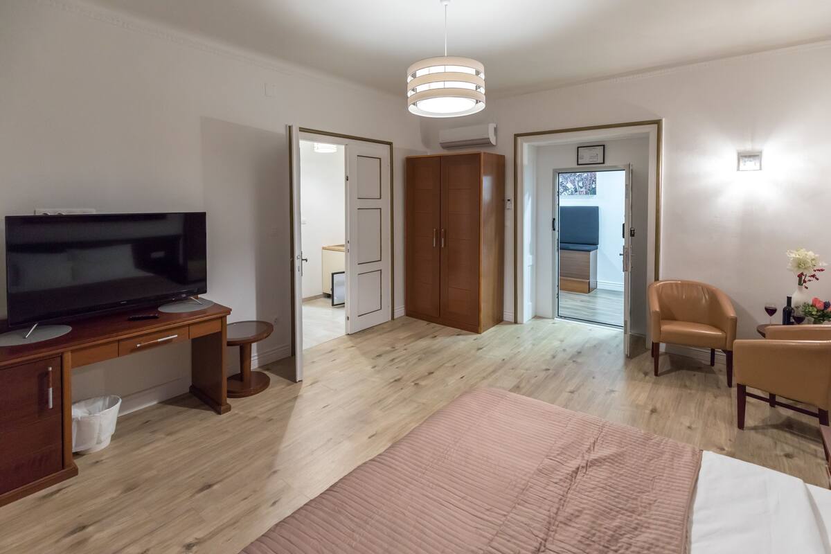 Een moderne hotelkamer met een houten bureau, een televisie, een bed met een roze sprei en een stoel.
