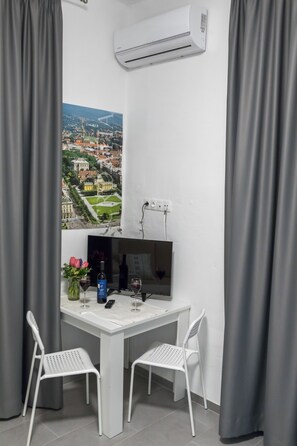 A small, modern room with a white table, two white chairs, a TV, and an air conditioning unit. - Bacu Apartments Zagreb (Zagreb)