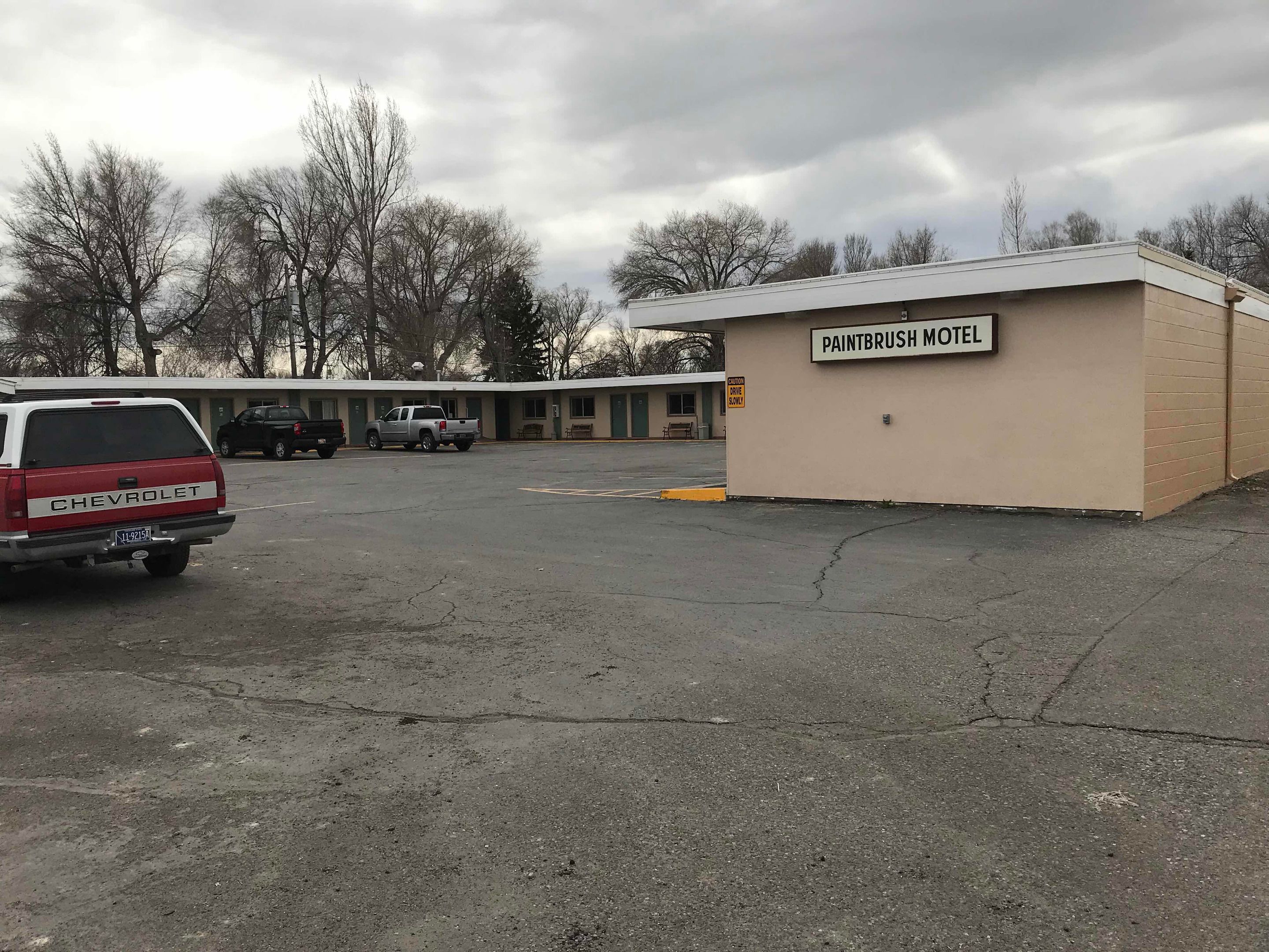 A motel with a sign reading "PAINTBRUSH MOTEL" and a parking lot with several vehicles.