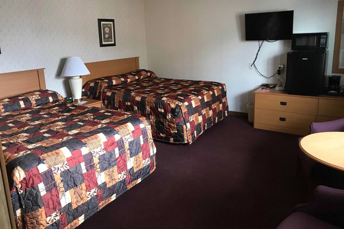 A hotel room with two beds, a TV, a microwave, a desk, and a chair.