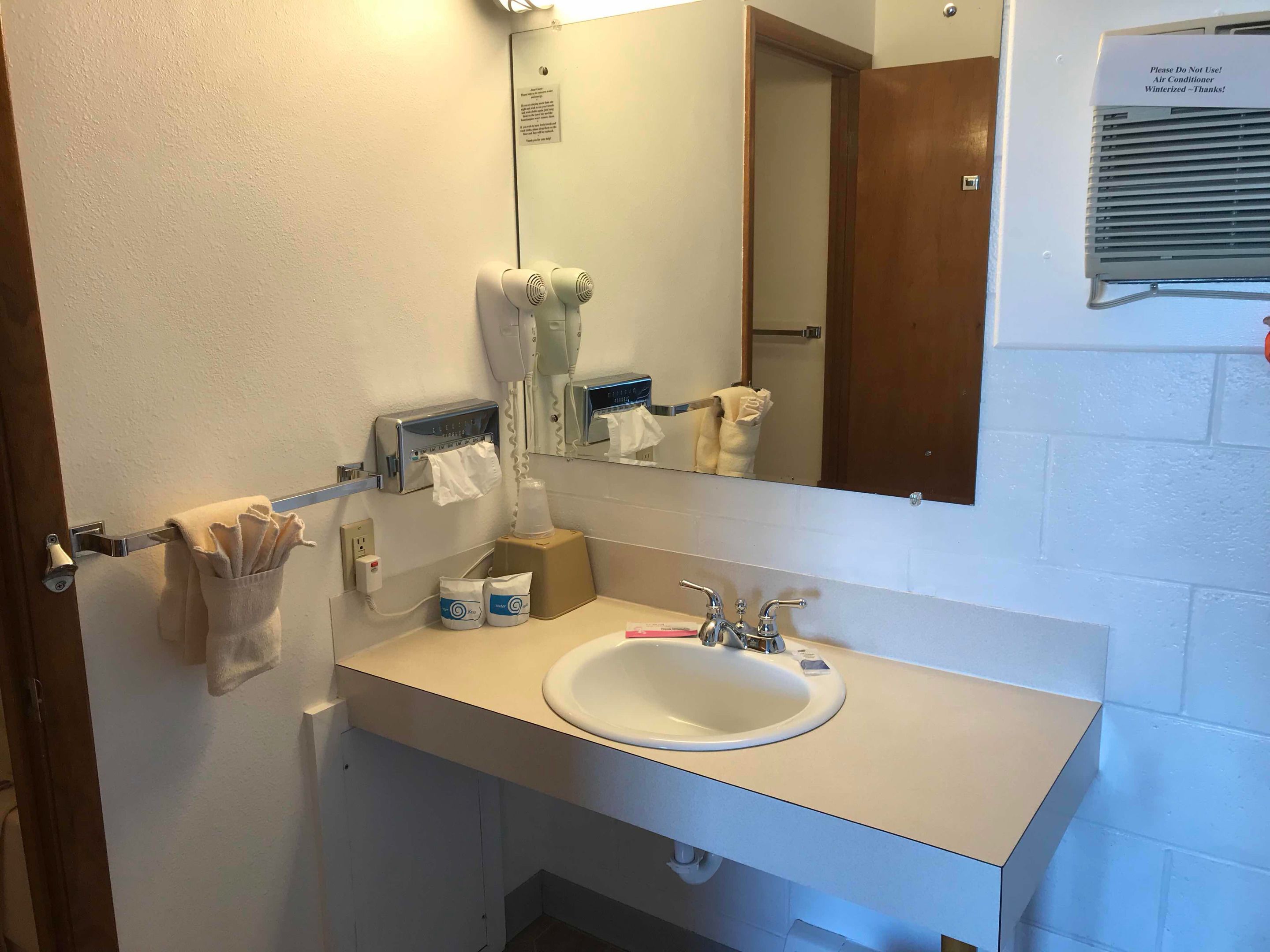 A hotel bathroom with a sink, towel rack, hand dryer, and a mirror.