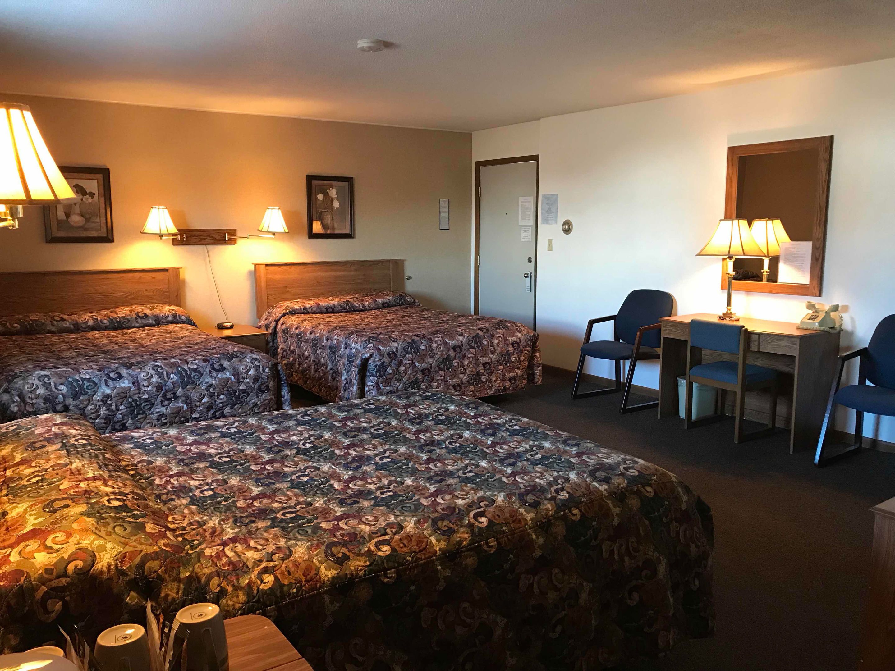 A hotel room with two beds, a desk, a chair, and a lamp.