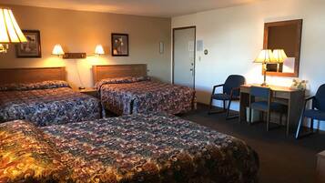 A hotel room with two beds, a desk, a chair, and a lamp.