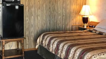 Ein Hotelzimmer mit Bett, Nachttisch, einer Schreibtischlampe, einer Mikrowelle und einem Kühlschrank.