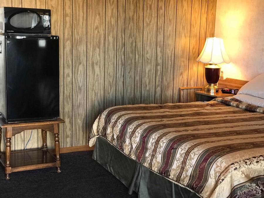 Ein Hotelzimmer mit Bett, Nachttisch, einer Schreibtischlampe, einer Mikrowelle und einem Kühlschrank.