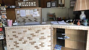 Un comptoir d’accueil avec une pancarte « BIENVENUE », divers panneaux d’information et une vitrine en verre contenant un livre.