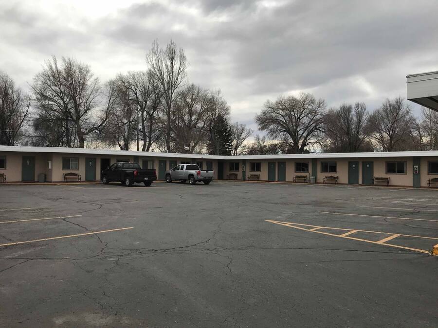 Un motel avec un parking, deux camions garés et une rangée de chambres aux portes vertes.