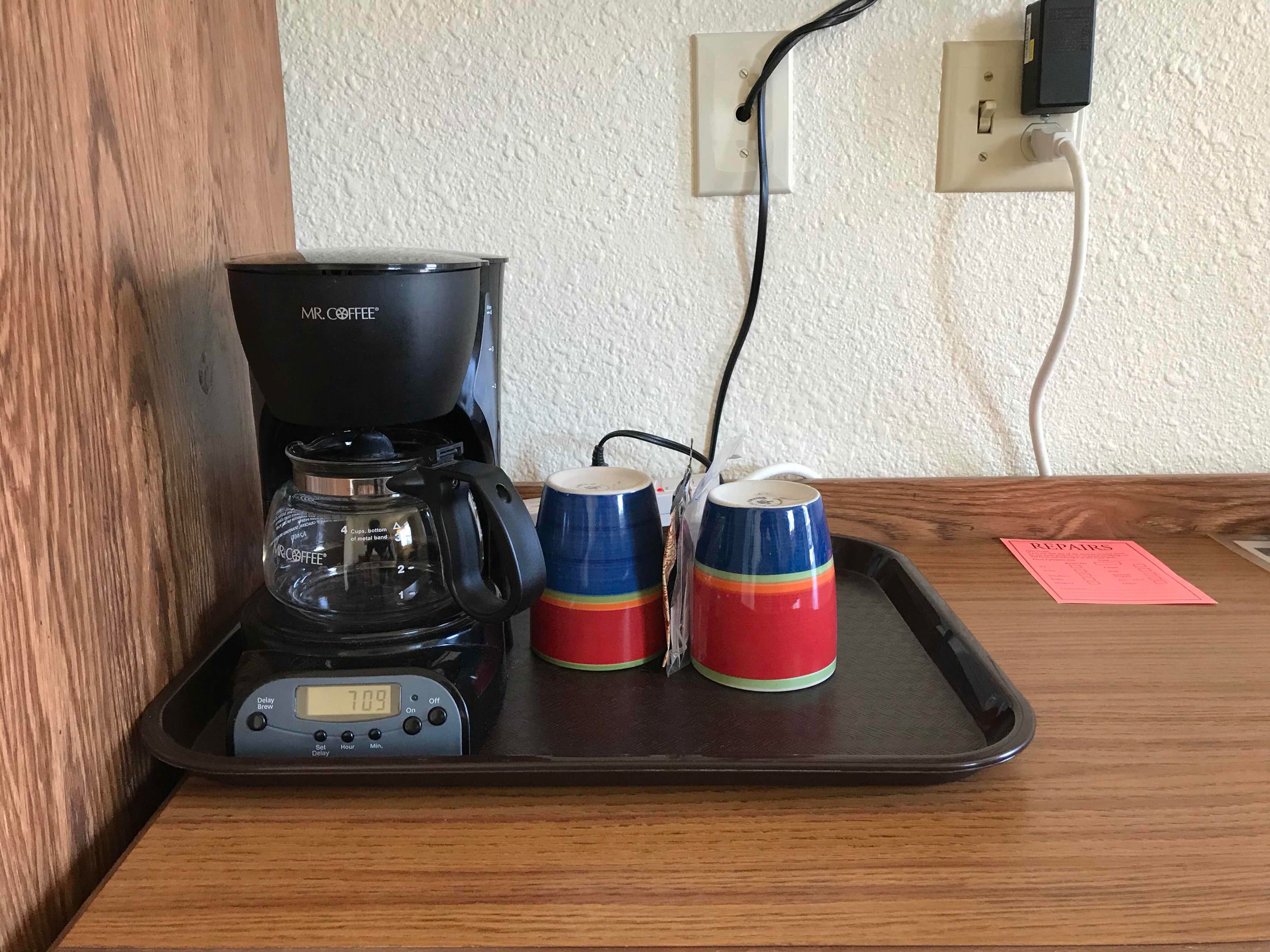 A coffee maker on a tray with two mugs on a wooden table.
