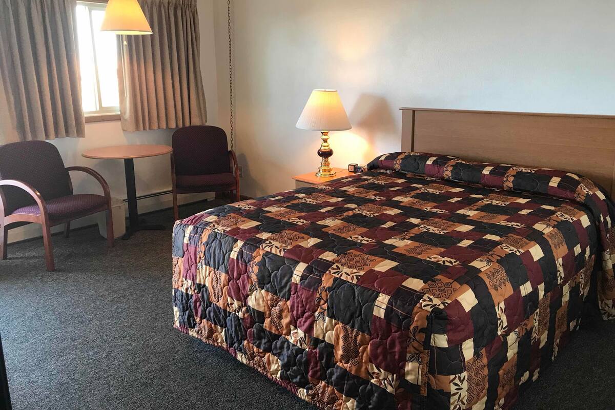 A hotel room with a large bed, a chair, a small table, and two lamps.