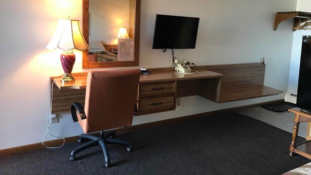 Une chambre d’hôtel avec un bureau en bois, une chaise, une télévision, une lampe et un miroir.
