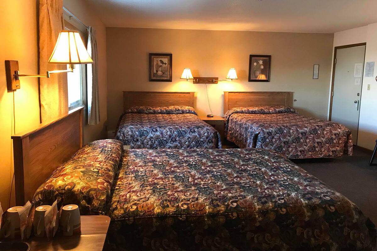 A hotel room with two beds, a wooden headboard, a nightstand, and a lamp.