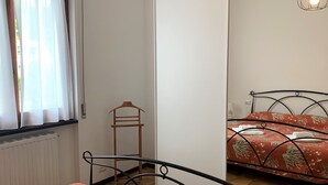 Quarto com cama, radiador, janela com cortinas e luminária suspensa.