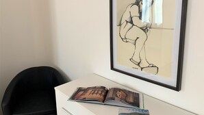 Obra de arte emoldurada retratando uma figura em uma escrivaninha, com um livro aberto e uma revista.