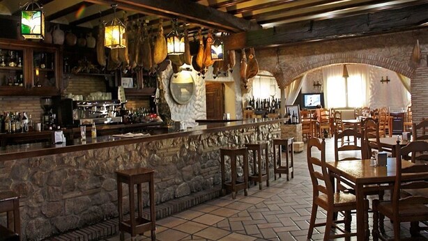 A rustic bar area with stone walls, wooden furniture, and hanging light fixtures. - Hotel El Seto (Motilla del Palancar)