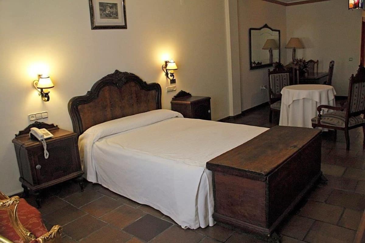 A hotel room with a large bed, two bedside tables with lamps, a small table with a chair, and a mirror on the wall.