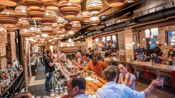 A bustling restaurant with a long bar and high, round, copper-colored pendant lights. - Downtown Luxury Suites (Jersey City)