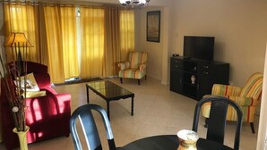 Una sala de estar con sofá, sillones, una mesa de centro, televisor y aparador.