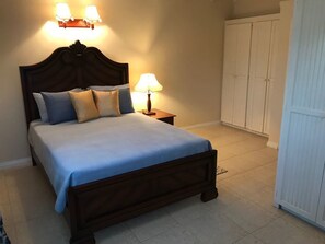A neatly made bed with a blue bedspread and pillows, a bedside lamp, and a wardrobe in the background.