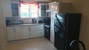 Una cocina compacta con armarios blancos, un refrigerador negro, un microondas y una estufa.