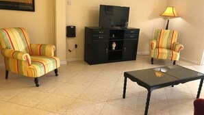 Una sala de estar con sillones a rayas, un mueble de entretenimiento negro, una mesa de centro de cristal y una lámpara.