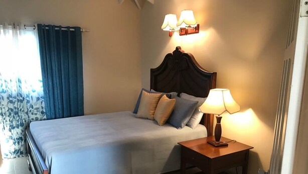 Una cama bien hecha con cabecera de madera, una mesita de noche con lámpara y una alfombra estampada en el suelo.