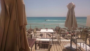 Une terrasse au bord de la plage, avec des tables et des chaises, une vue sur la mer et des parasols.