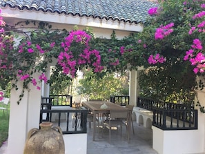 Un patio al aire libre con una mesa y sillas de madera, rodeado por un muro blanco y un techo de tejas.