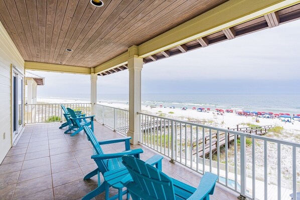 A covered balcony with blue chairs, a view of the beach, and a wooden ceiling.