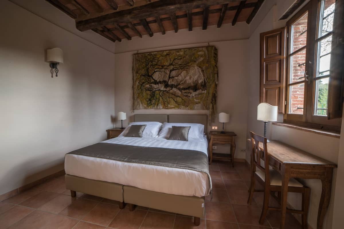 A bedroom with a large bed, a desk, and a window with a view of the outside.