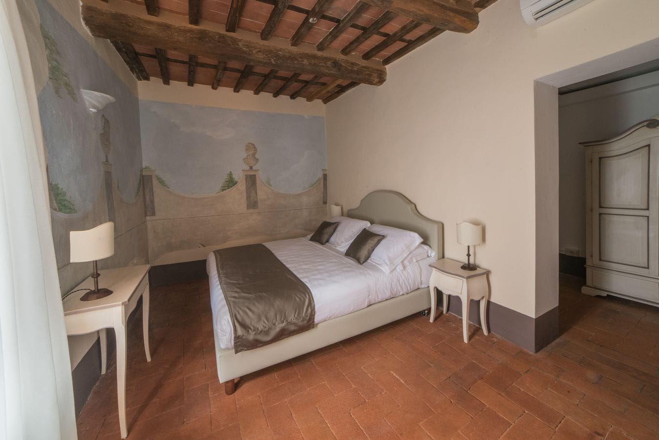 A bedroom with a bed, two bedside tables with lamps, a wardrobe, and a mural on the wall.