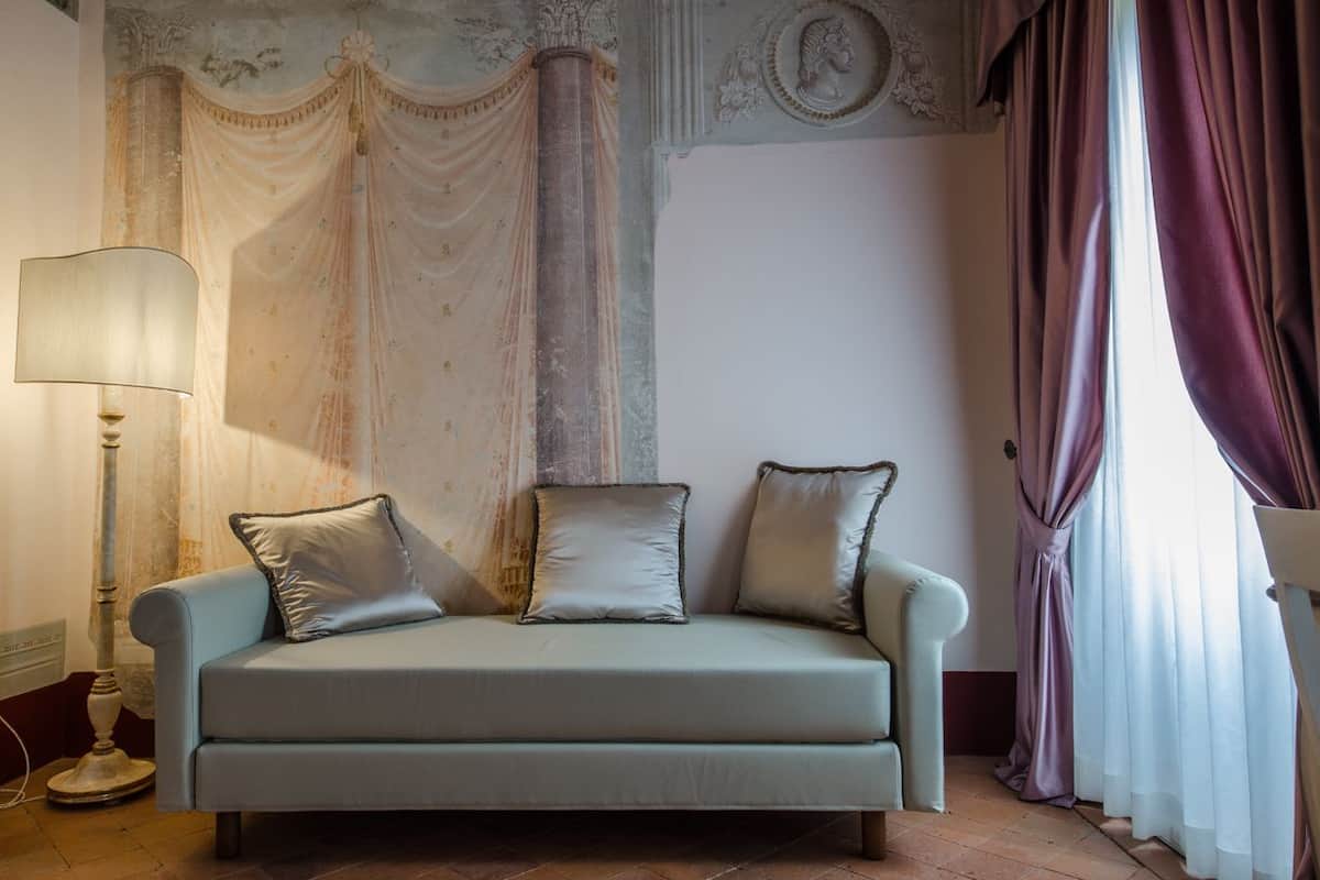 A room with a light-colored sofa, a floor lamp, and a large window with purple curtains.