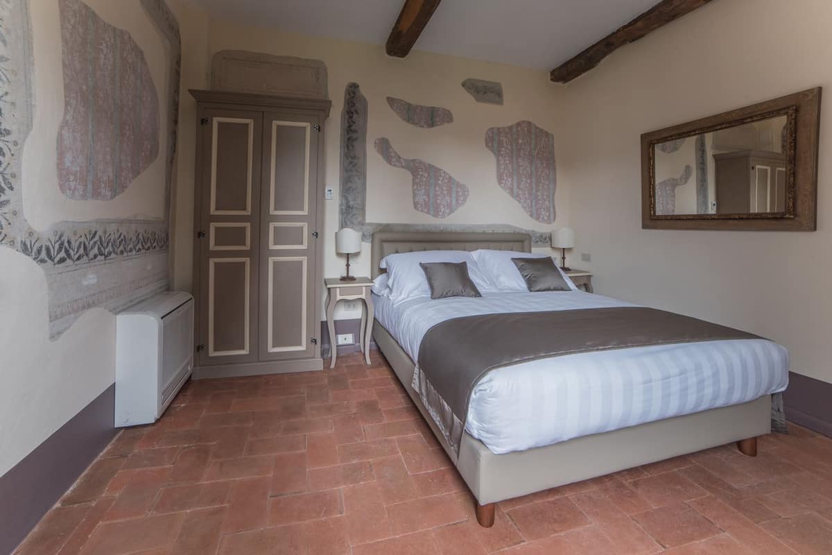 A bedroom with a bed, nightstands, a mirror, and a radiator.