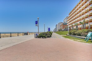 Un hotel frente al mar con un paseo marítimo de ladrillo rojo, palmeras y un cielo azul despejado.