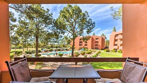 Ein Balkon mit zwei Stühlen und einem Tisch, der auf einen Pool und ein Gebäude mit mehreren Balkonen blickt.