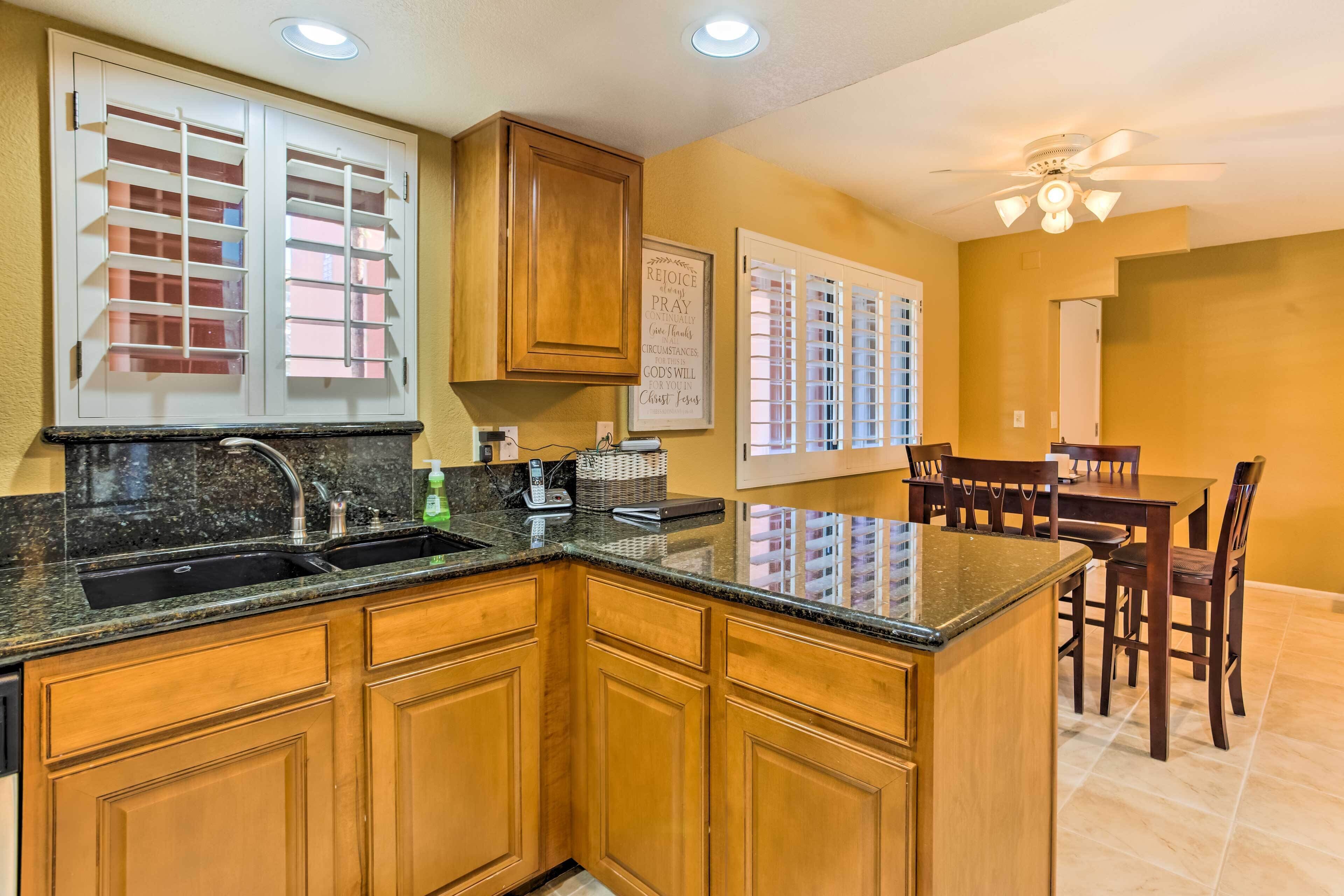 A kitchen with wooden cabinets, a granite countertop, a sink, and a dining area with a table and chairs.
