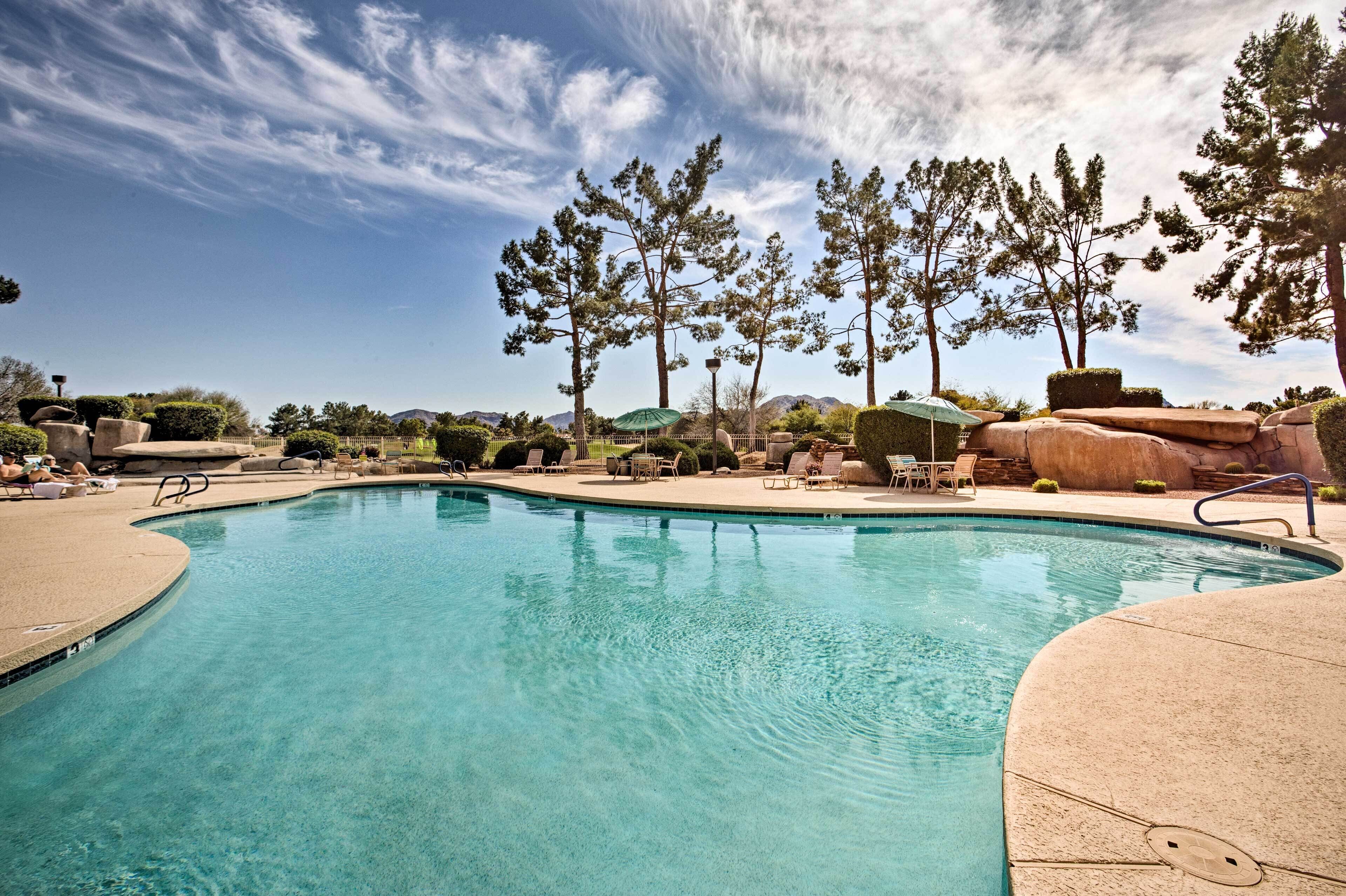 A clear swimming pool with lounge chairs and umbrellas, surrounded by trees and mountains in the background.